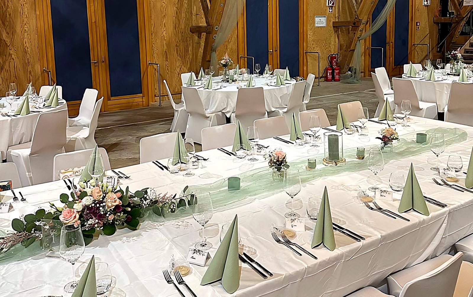 Festlich gedeckte Tafel mit weißen Hussen, salbeigrünen Servietten und Blumengesteck